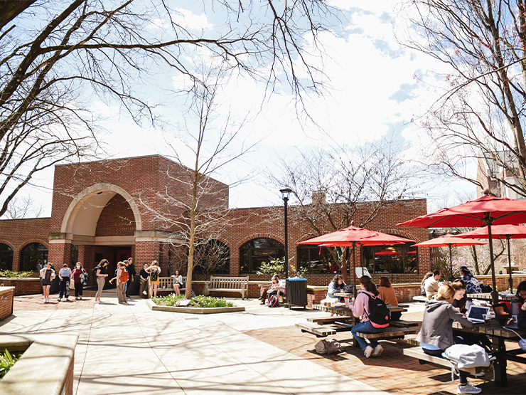 Students gather in groups or sit around tables in Parents Plaza, an open plaza in front of Seegers Union, a brown brick building.